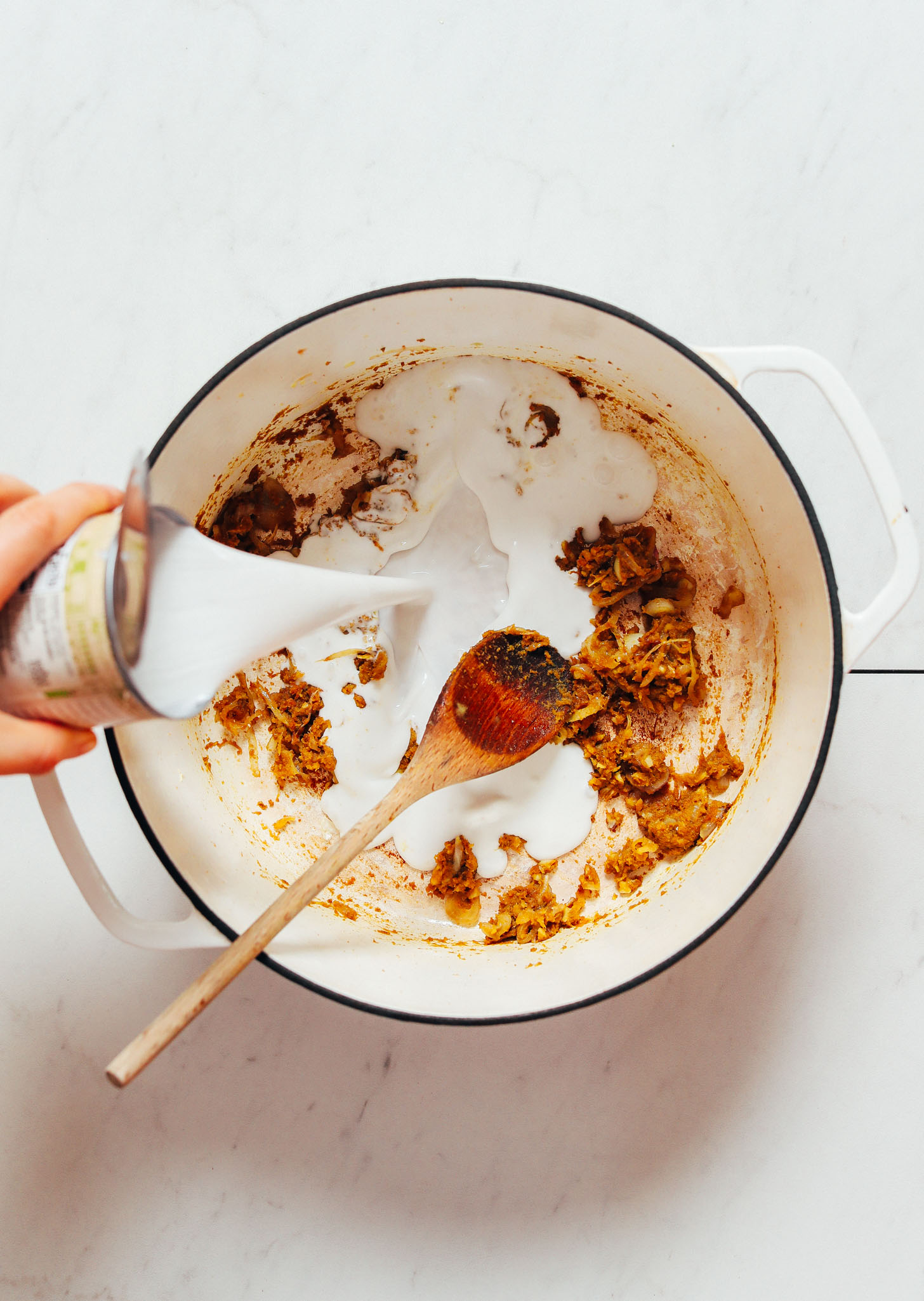 Pouring a can of coconut milk into a pot of spices for making Thai-Inspired Chicken Noodle Soup