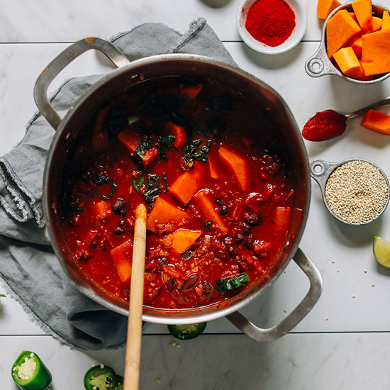 Wooden spoon in a pot of Butternut Squash Chili alongside ingredients used to make it