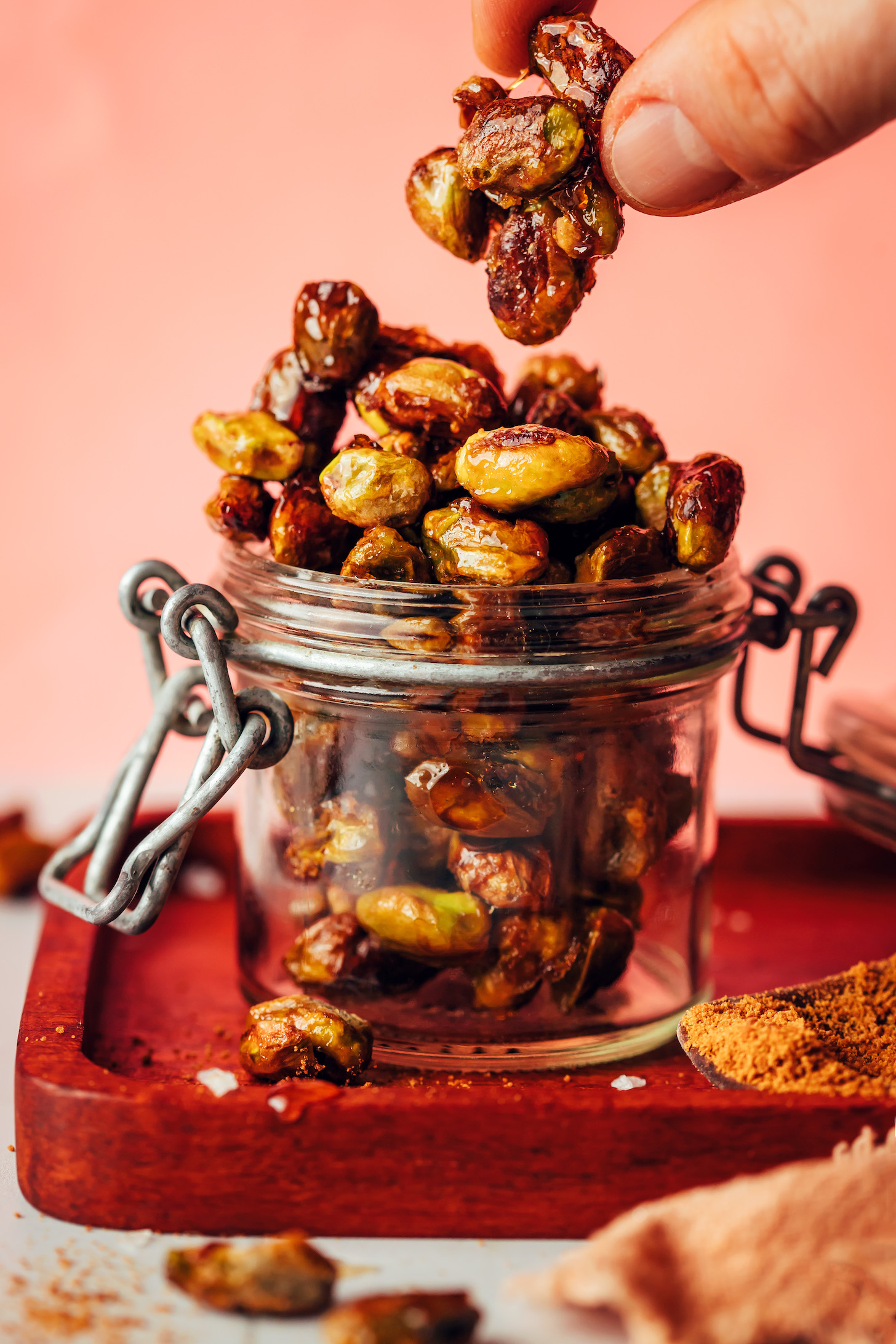 Holding up a cluster of candied pistachios above a jar with more of them