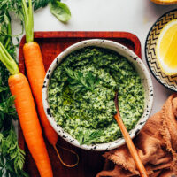 Carrots next to a bowl of carrot top pesto