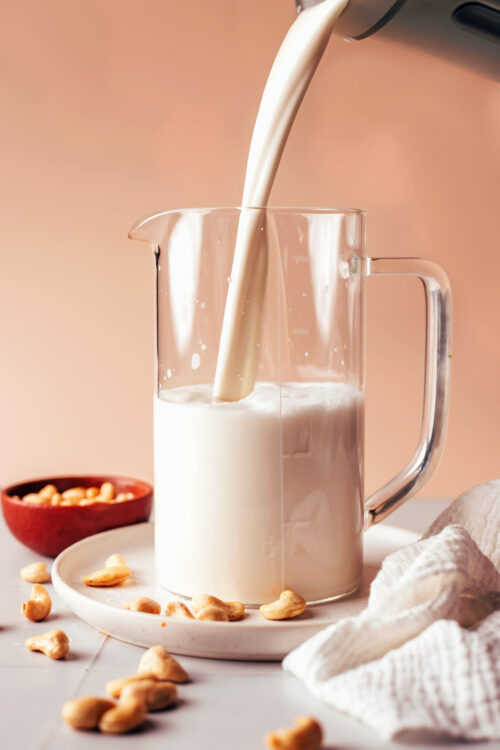 Pouring homemade cashew milk into a pitcher