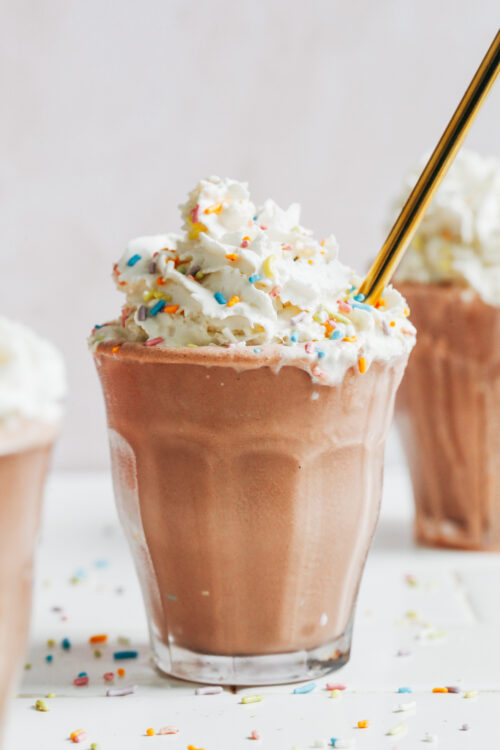 Glasses filled with our vegan chocolate milkshake and topped with dairy-free whipped cream and sprinkles