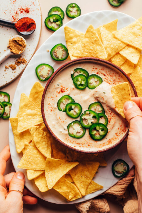 Dipping a tortilla chip into a bowl of vegan white bean queso