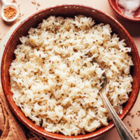 Spoon in a bowl of fluffy jeera rice with spices around it