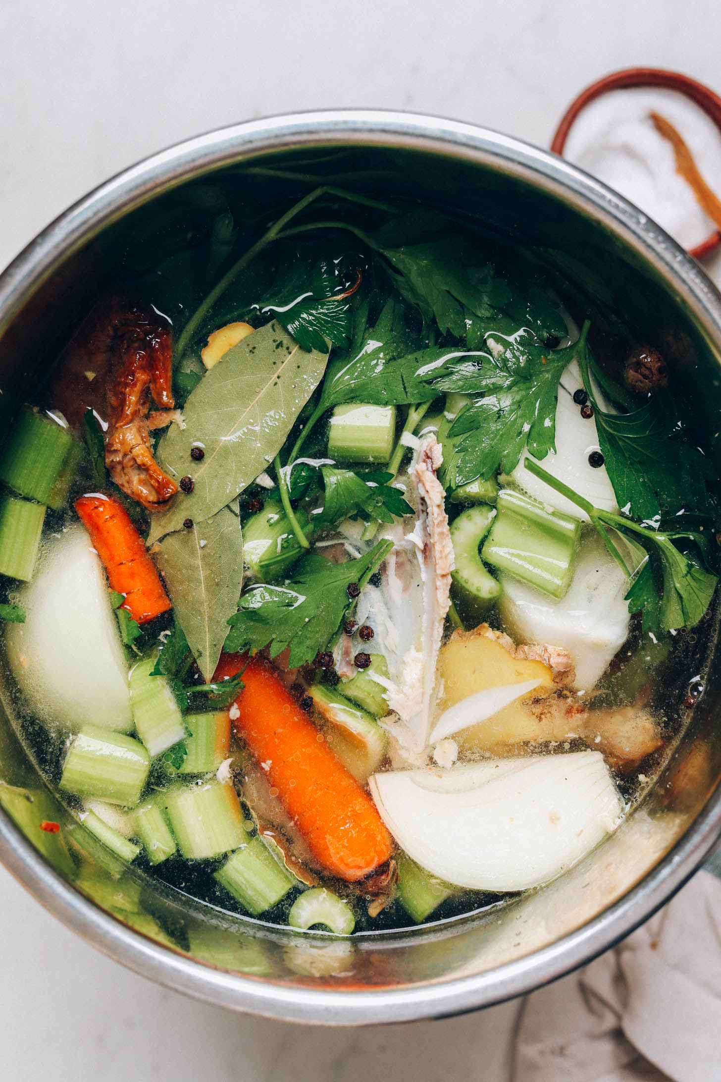 Chicken bones, onions, garlic, celery, carrots, ginger, bay leaves, black pepper, parsley, and water in an Instant Pot