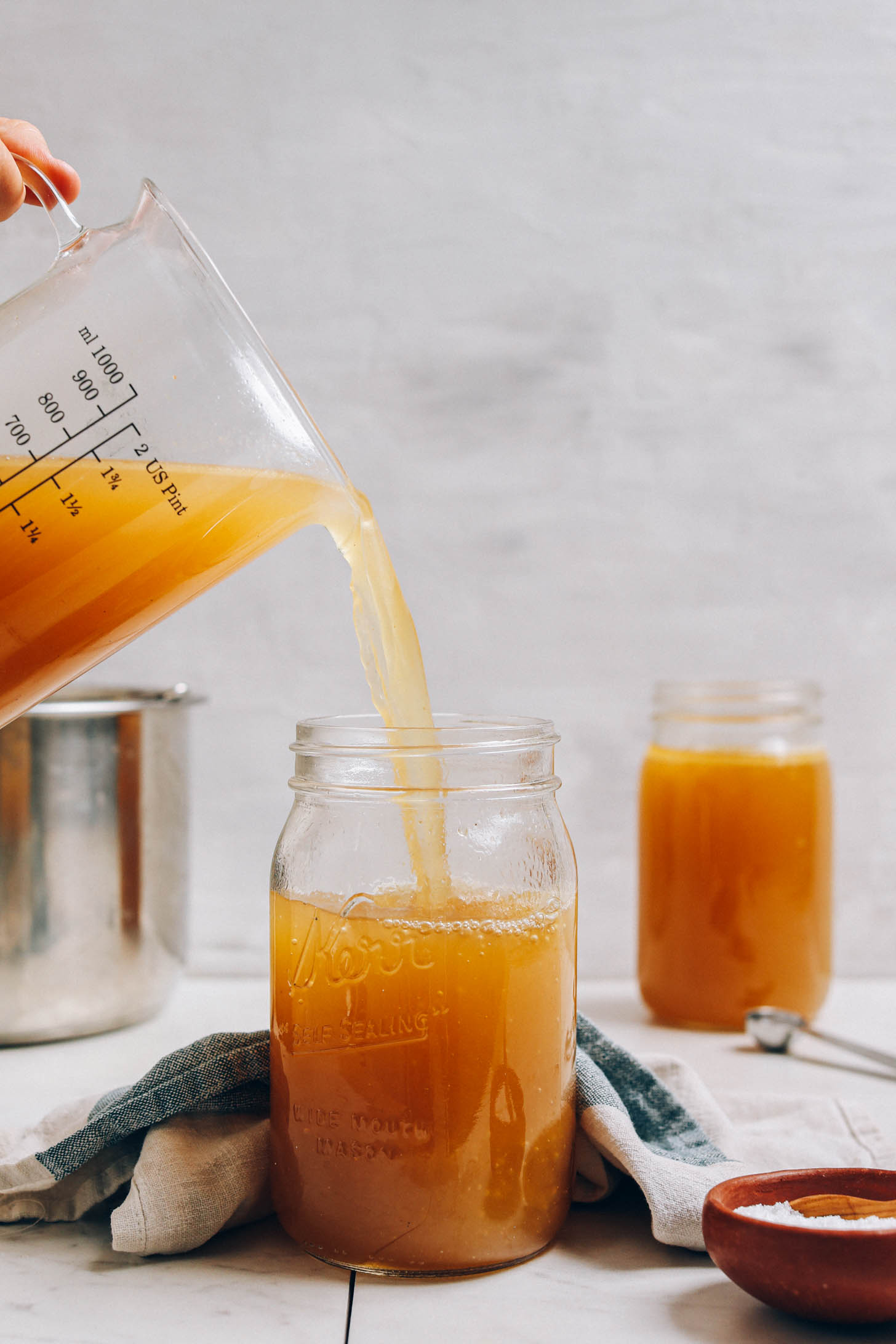 Pouring homemade chicken stock into a quart-size jar