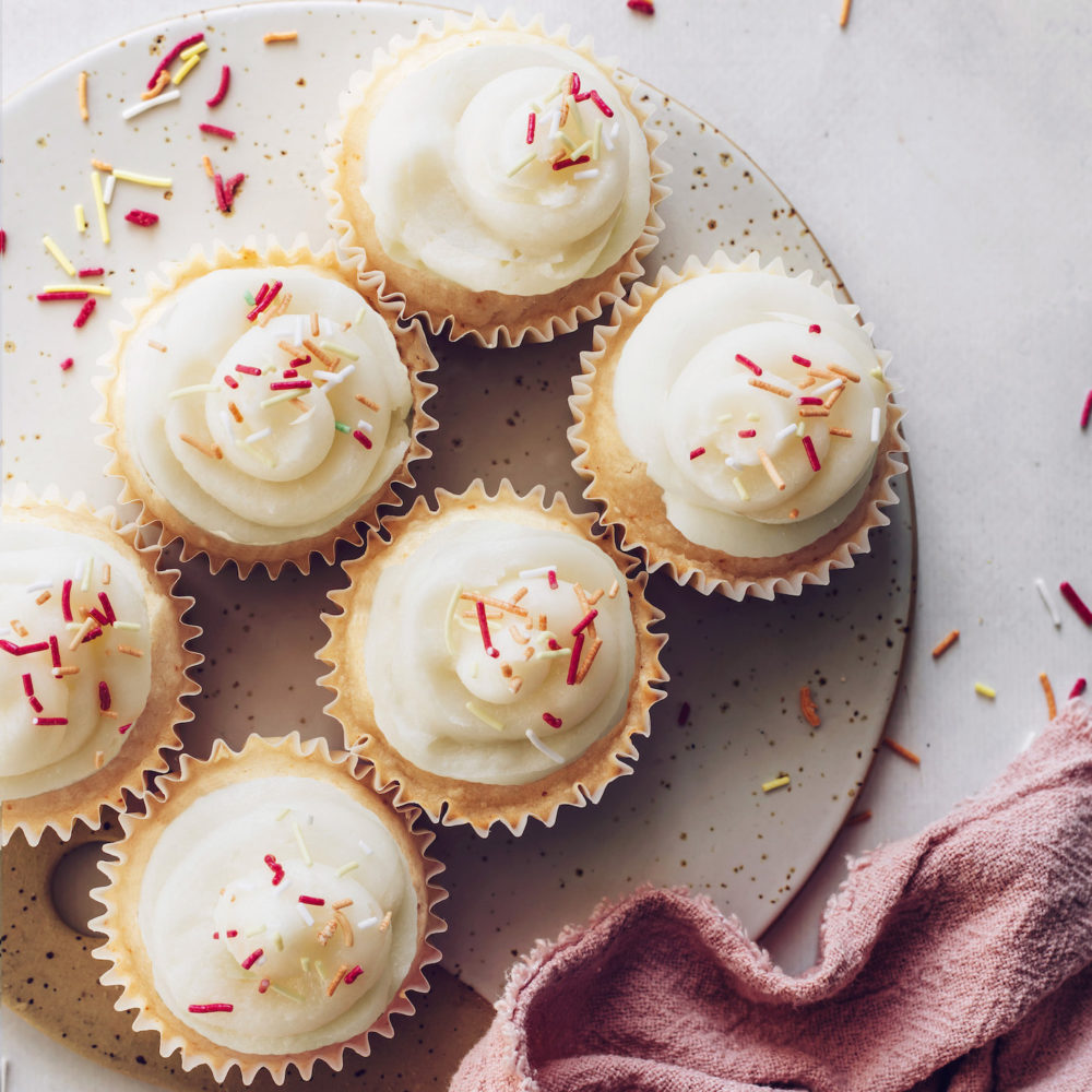 Top down shot of six vegan vanilla cupcakes topped with frosting