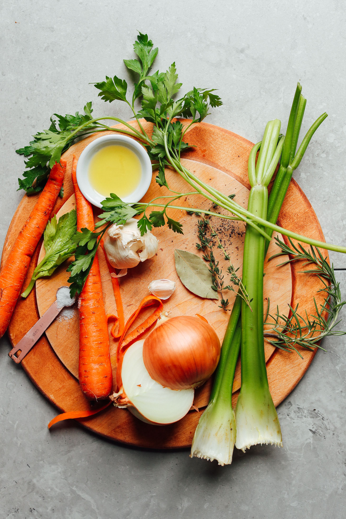 Onions, carrots, celery, fresh herbs, garlic, bay leaf, salt and olive oil on a cutting board ready to make the BEST vegetable broth recipe