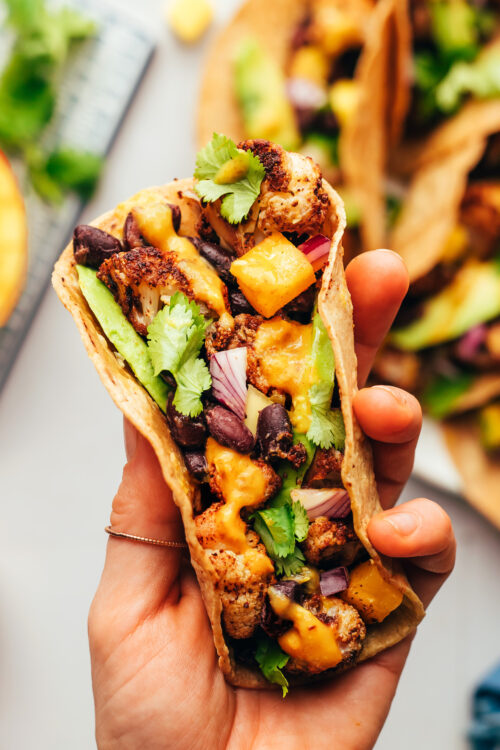 Holding up a vegan jerk cauliflower taco topped with avocado and mango hot sauce