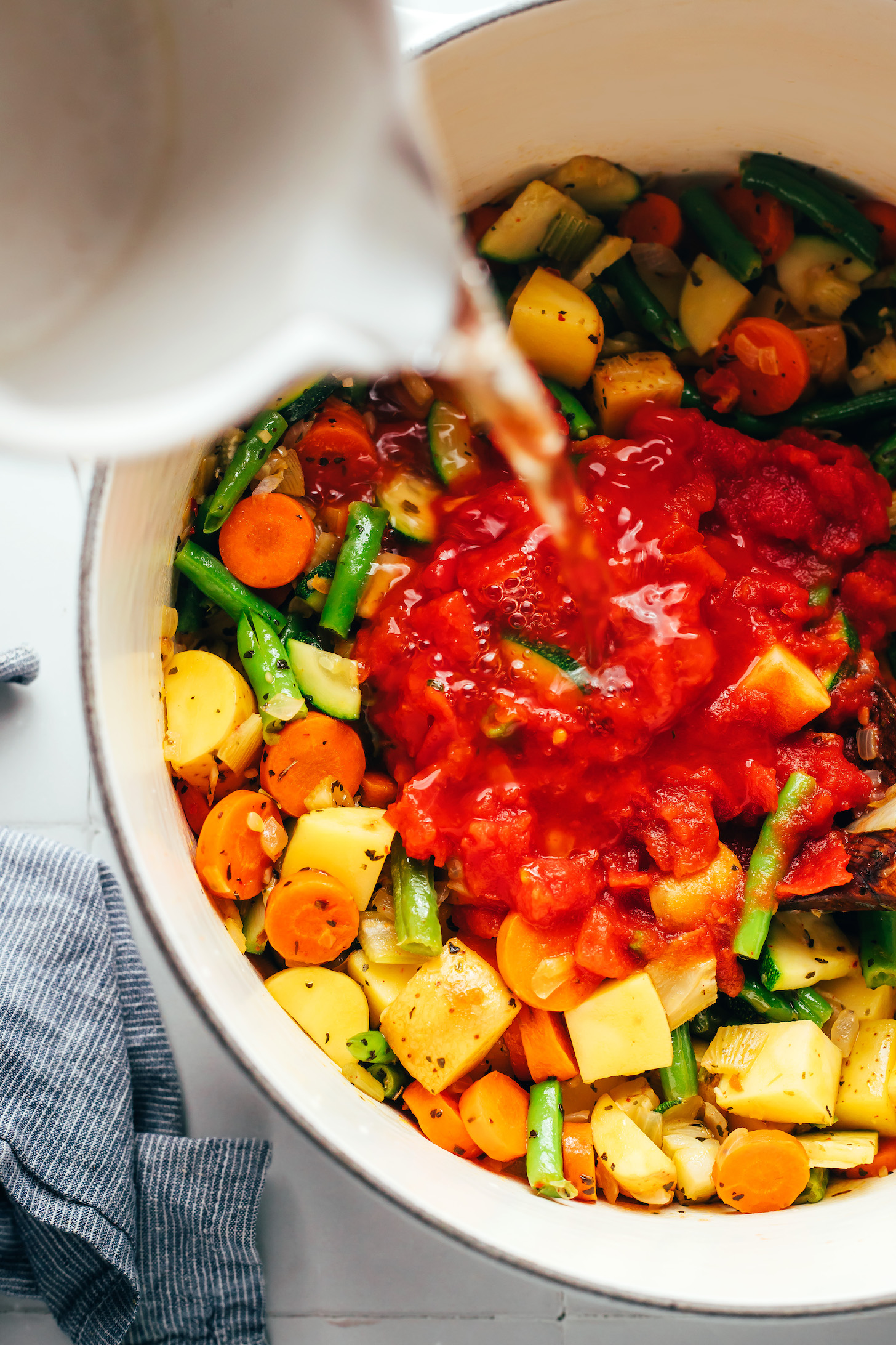 Pouring water over crushed tomatoes in a pot with sautéed veggies