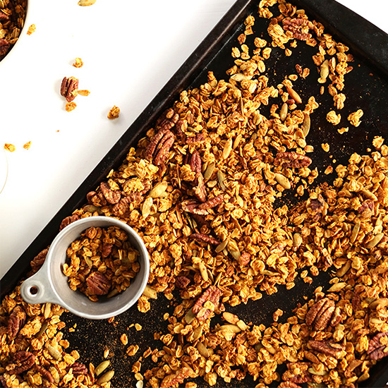 Measuring cup and baking sheet of homemade Maple Pumpkin Pecan Granola