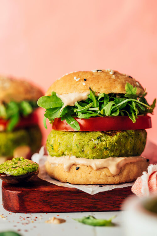 Side view of a pesto veggie burger on a bun with arugula, tomato, and balsamic aioli