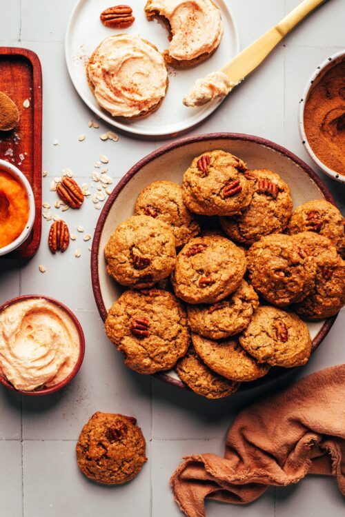 Plates of unfrosted and frosted pumpkin oat cookies next to ingredients used to make them