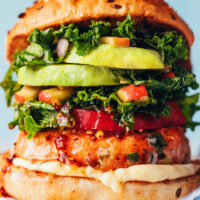 Close up photo of a loaded salmon burger with mayonnaise, tomato, kale apple slaw, and avocado