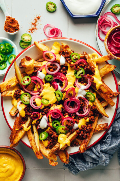 Bowl of vegan chili cheese fries topped with homemade vegan cheddar, jalapeño, and pickled onions