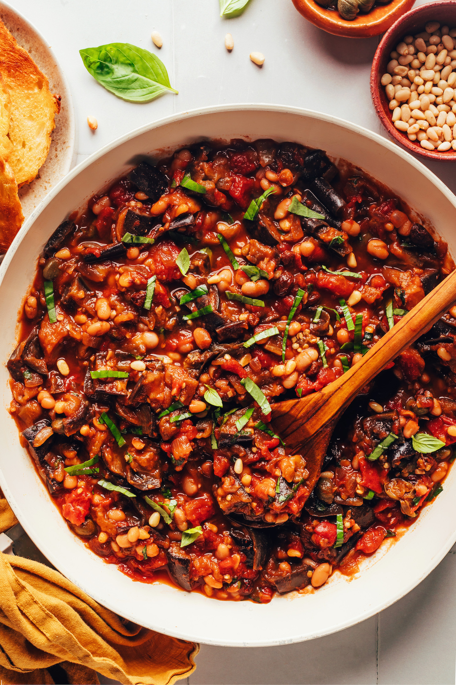 Wooden spoon resting in a skillet of white bean eggplant caponata